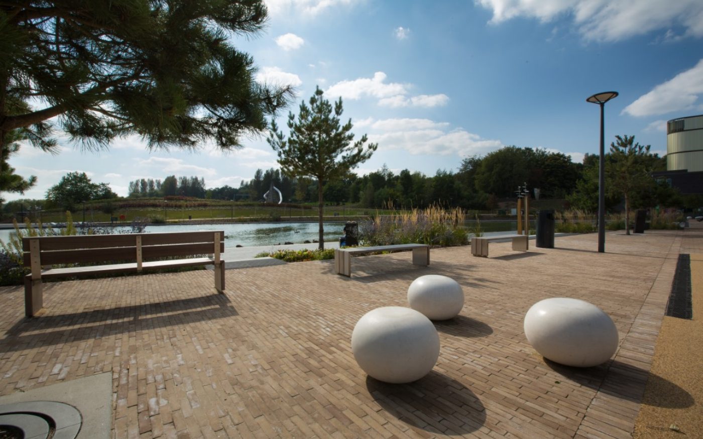 Benches and modern sculptures on paved landscaping by lake with trees