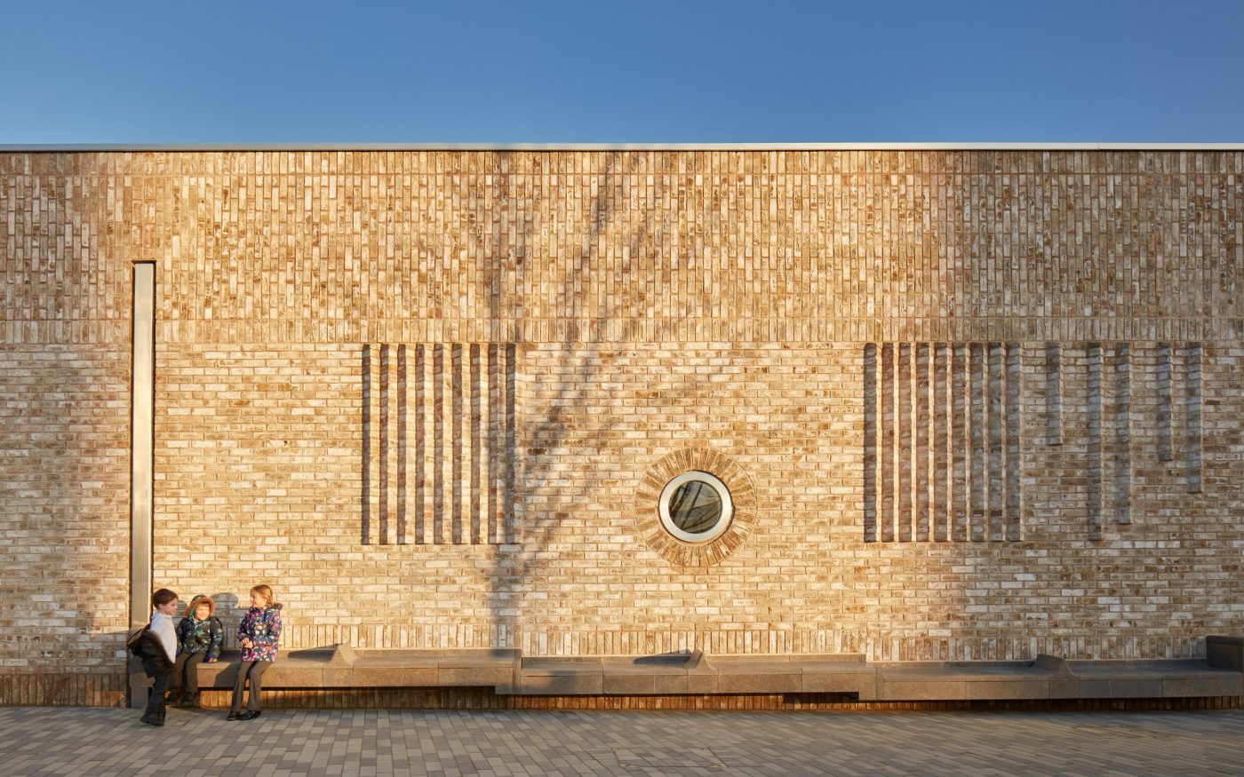 three children sat on bench outside the eye-catching brick wall design with circular windows