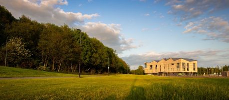 Green field and trees with blue sky, modern brick building in the distance