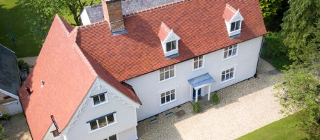 Aerial view of large old house with red tile roof in green surroundings