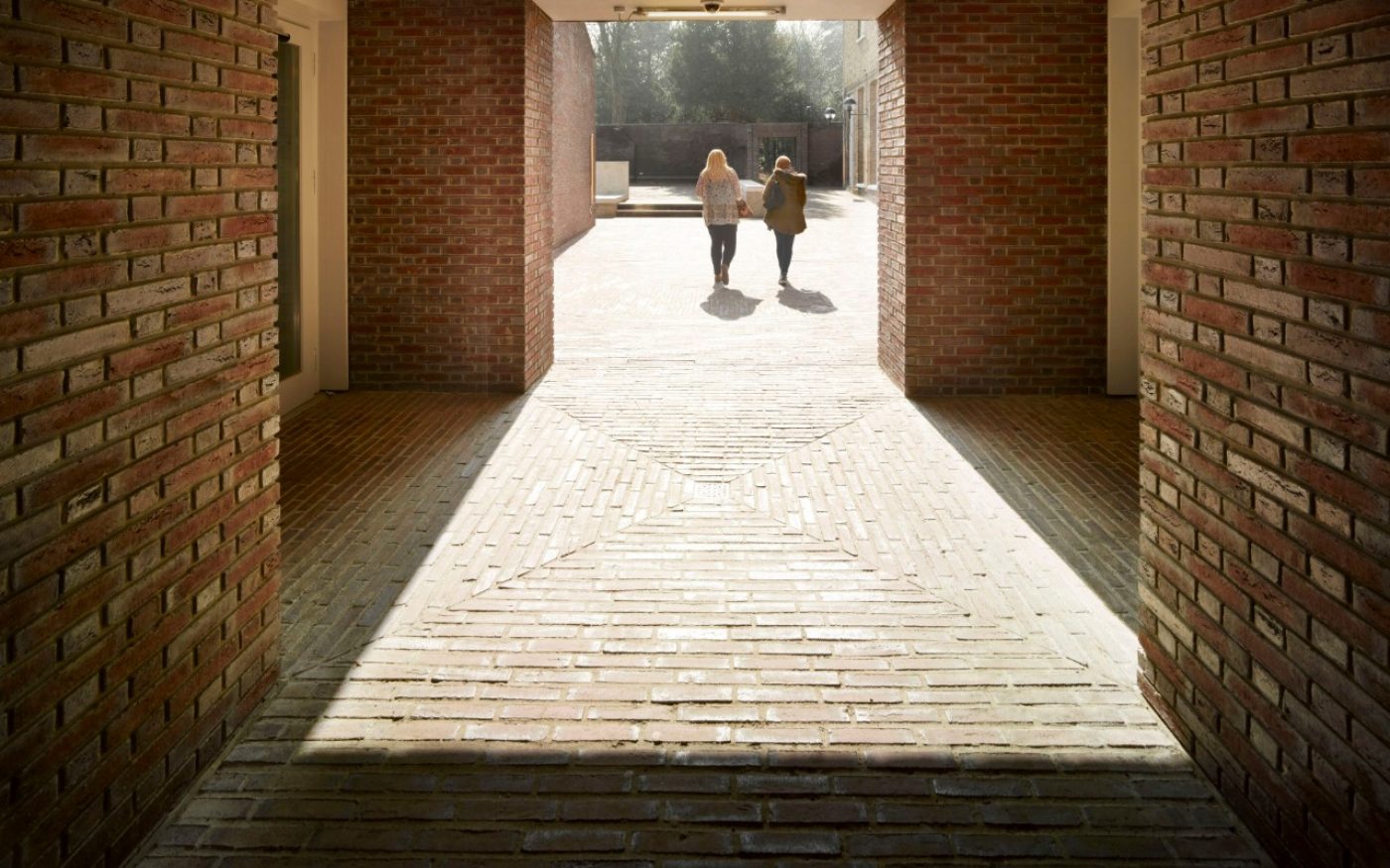 Two students walking away in the distance down red paved path
