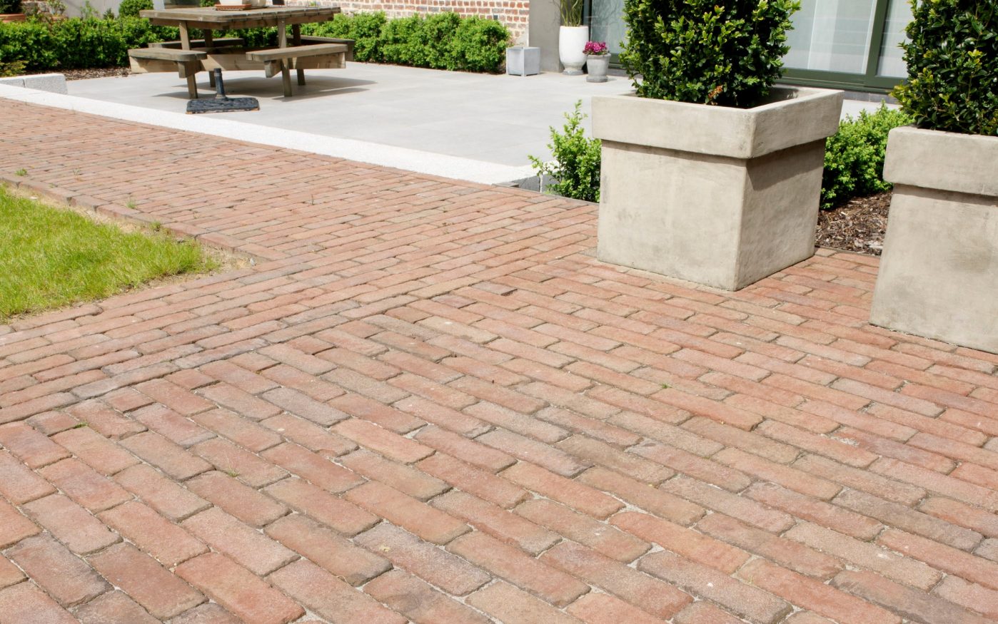 Red clay pavers with large plant pots and a park bench in the background