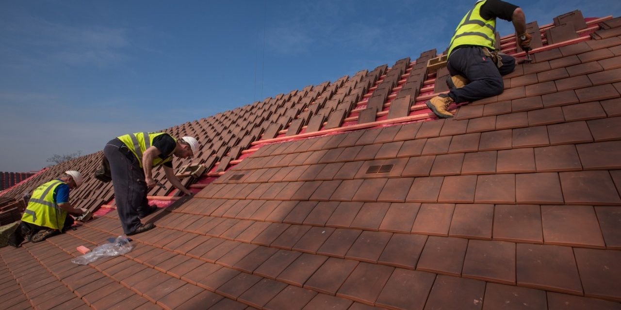 three workmen laying clay roof tiles on a property