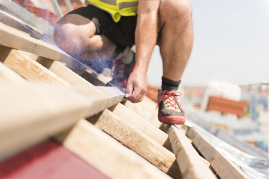 Urban roofer applying marks on wooden bars with chalk line bare hands wearing safety jacket in an urban location
